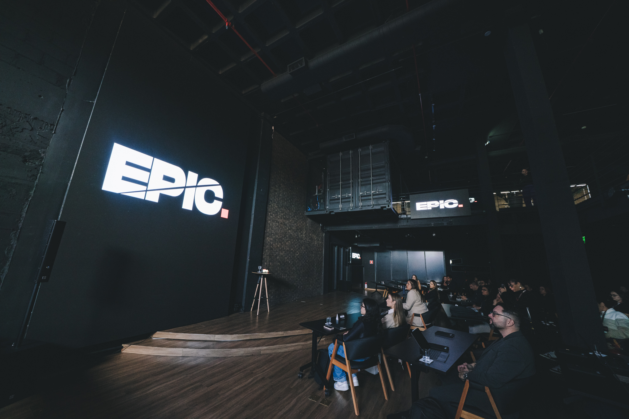 An empty stage with the EPIC logo projected in giant letters on the wall; the audience at Jornada Exponencial 2025 waiting